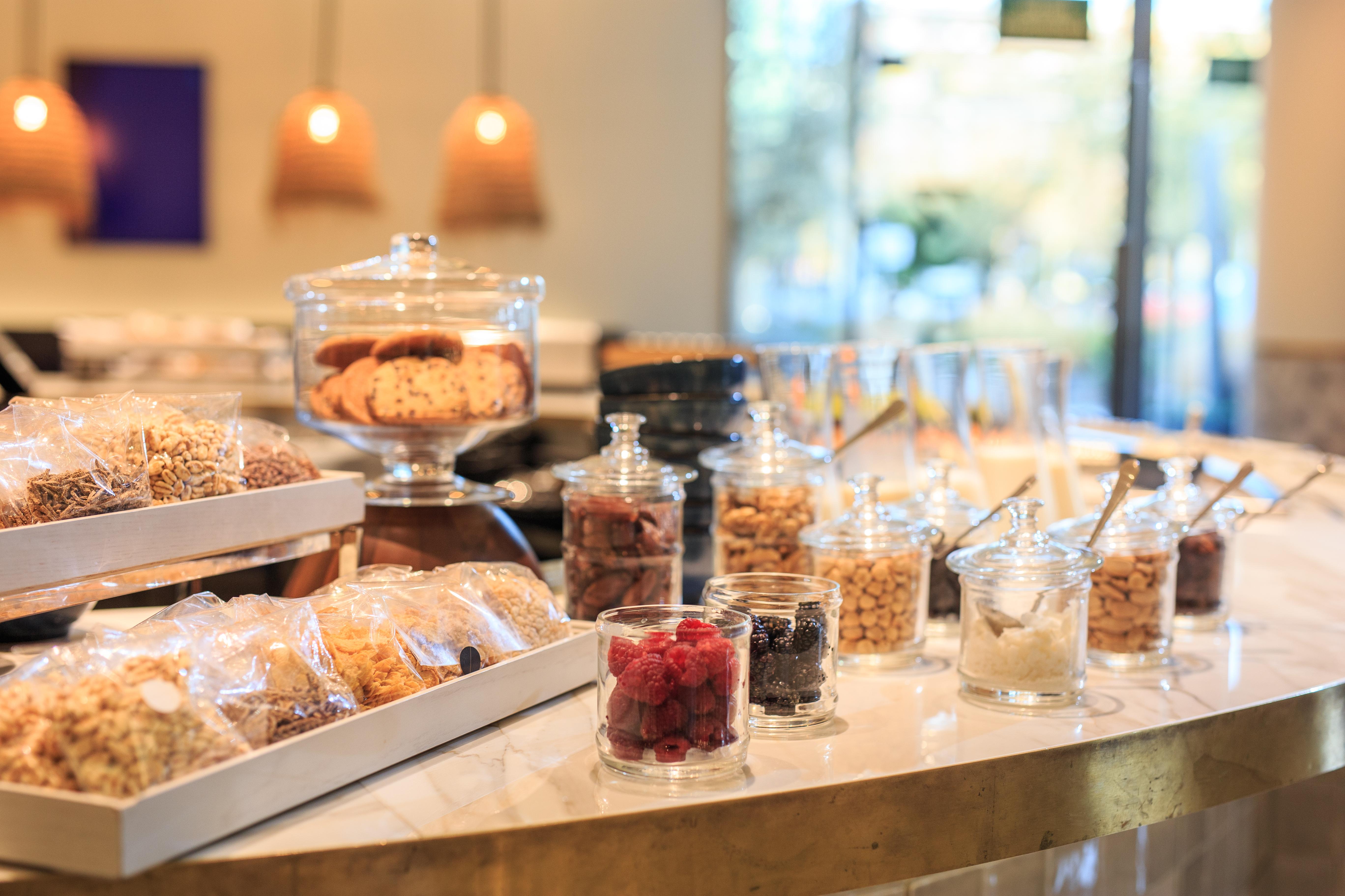 Grand Hyatt Barcelona Ξενοδοχείο Εξωτερικό φωτογραφία The photo displays a variety of snacks and treats arranged on a countertop. There are several jars filled with different types of items, including colorful candies, nuts, and dried fruits. A glass container holds cookies, and there are neatly package