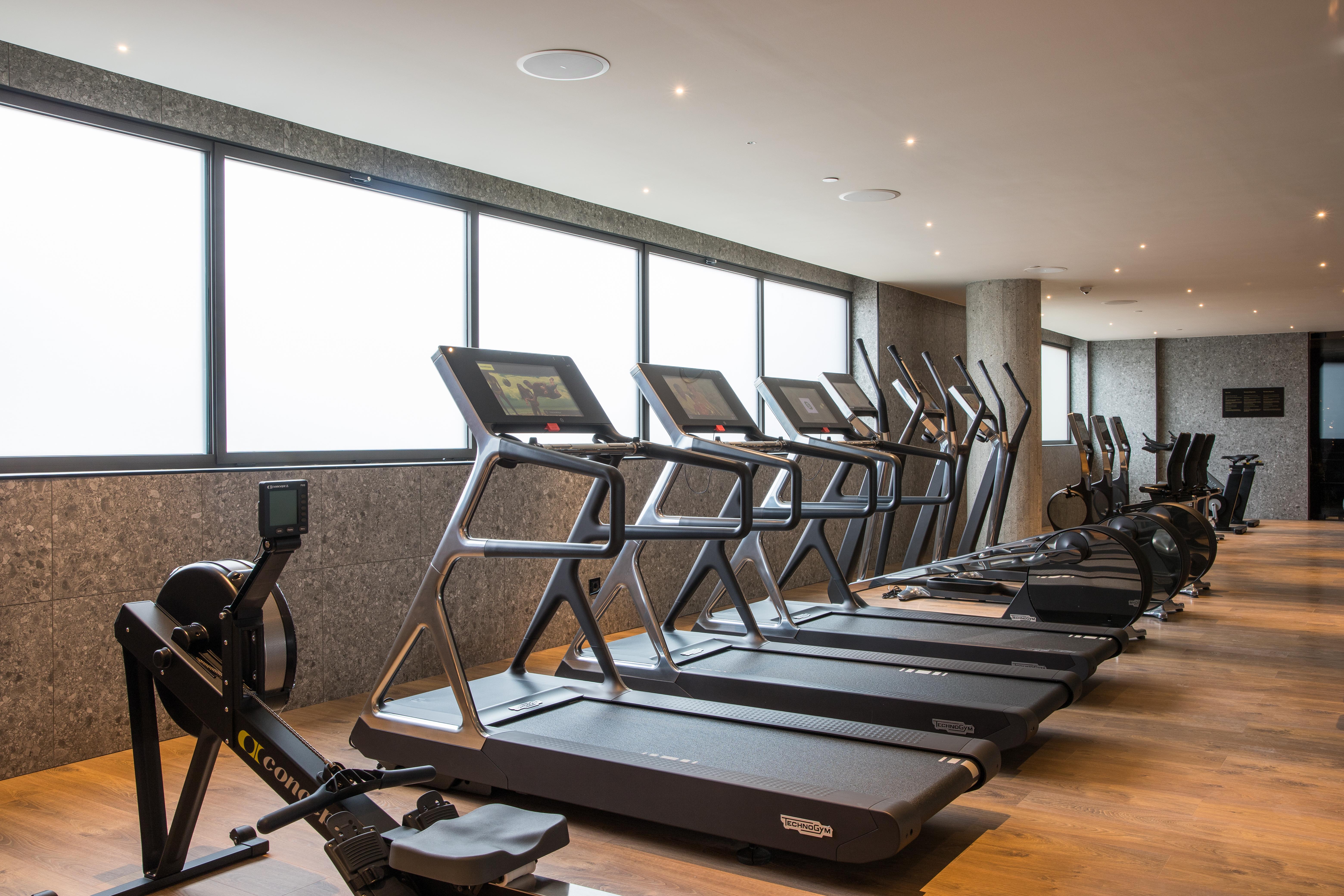 Grand Hyatt Barcelona Ξενοδοχείο Εξωτερικό φωτογραφία The photo shows a modern gym space featuring several pieces of exercise equipment. In the foreground, there are treadmills, while in the background, there are elliptical machines lined up against large windows that provide natural light. The flooring