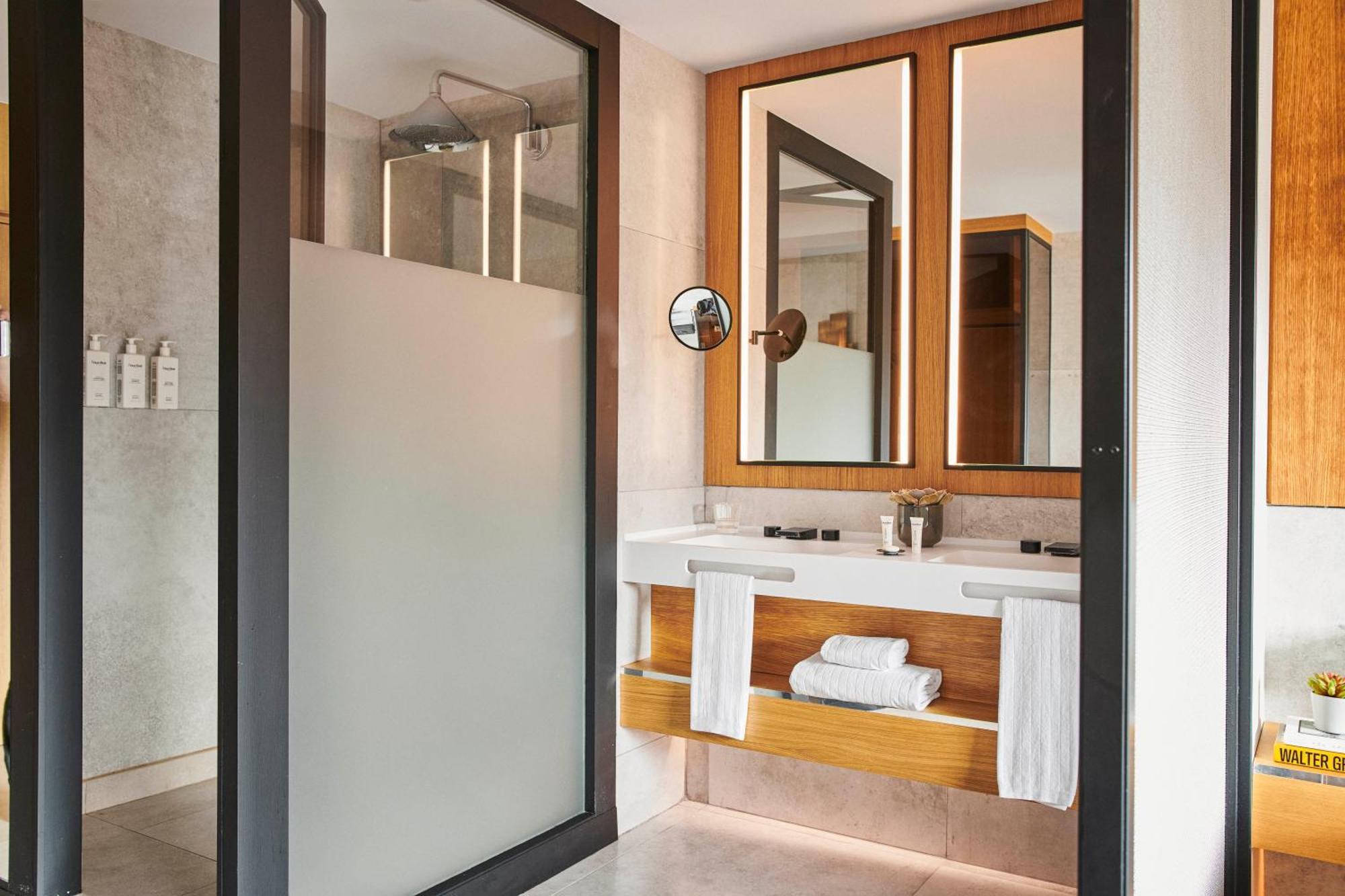 Grand Hyatt Barcelona Ξενοδοχείο Εξωτερικό φωτογραφία The photo shows a modern bathroom. 

- On the left, there is a glass shower enclosed by a frosted panel, suggesting privacy.
- In front of the shower, there is a vanity with a sink.
- Above the sink, there are two large mirrors framed with wooden bor
