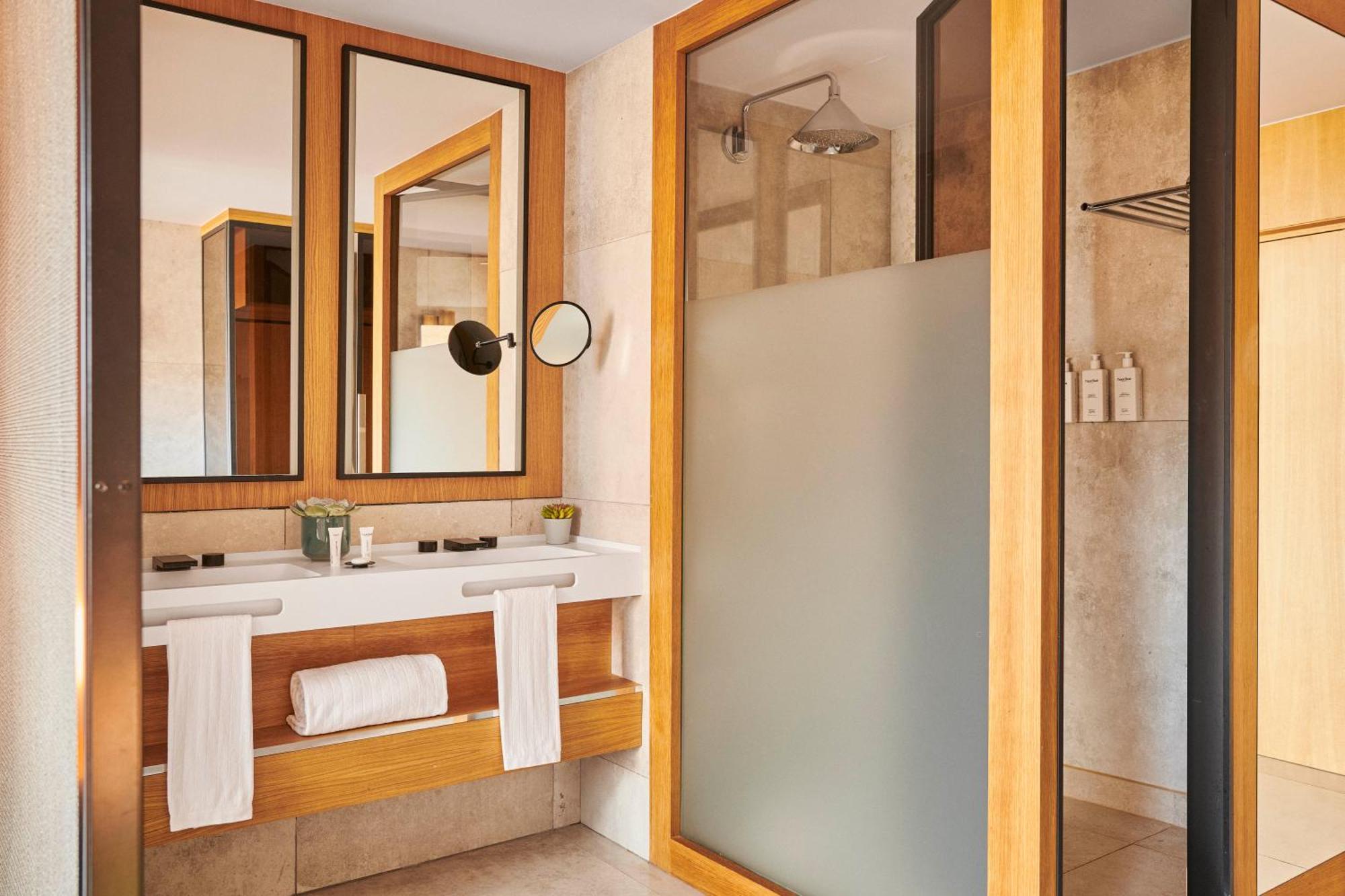 Grand Hyatt Barcelona Ξενοδοχείο Εξωτερικό φωτογραφία The photo depicts a modern bathroom featuring a combination of natural materials and sleek design. There are three mirrors mounted on the wall above a wooden vanity. The vanity includes a basin and is adorned with toiletries and a small plant. On the
