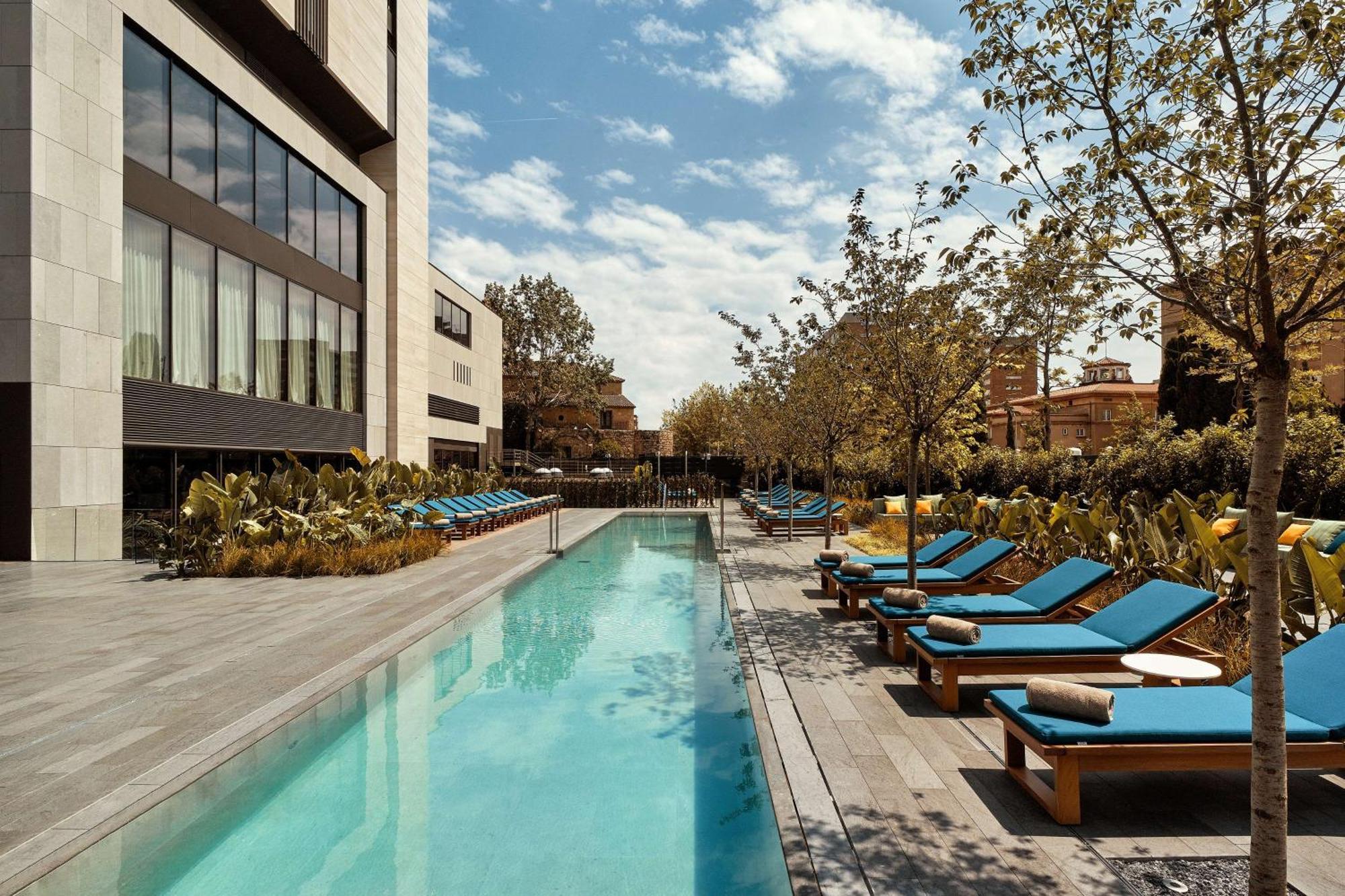 Grand Hyatt Barcelona Ξενοδοχείο Εξωτερικό φωτογραφία The photo showcases a modern outdoor pool area. In the foreground, there is a long, rectangular swimming pool with clear blue water. Surrounding the pool are lounge chairs with bright blue cushions, arranged neatly along both sides. The area features